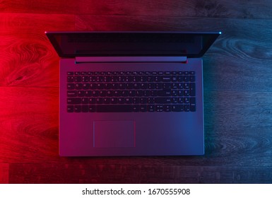 Modern Laptop On A Wooden Floor With Blue Red Neon Light. Gradient Glow. Gaming Concept. Top View