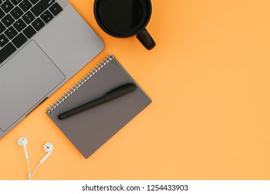 Modern Laptop, White Headphones, Gray Notebook With A Pen And A Cup Of Coffee On The Orange Background And A Place For Text, A View From Above. Flatlay Copyspace.