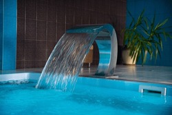 A Modern Large Indoor Pool With Blue Lighting And A Waterfall
