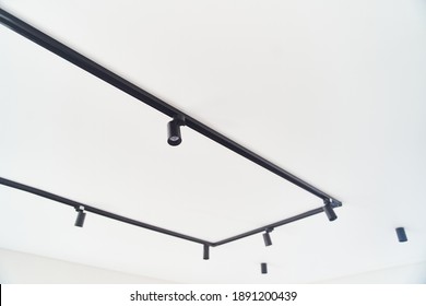 Modern LED black track spot lights in the interior. Hanging lamps spotlights attached to a concrete ceiling in an office loft room