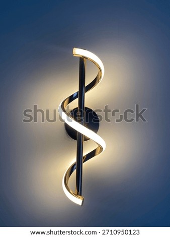 A modern LED wall light featuring a sleek spiral design, mounted on a smooth wall. The warm white illumination creates a soft ambient glow, highlighting the elegant curves and metallic accents.
