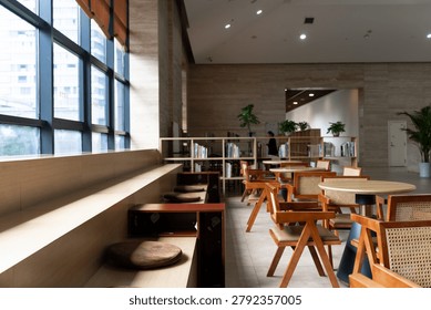 Modern library reading area featuring wooden tables, rattan chairs, and bookshelves bathed in natural light