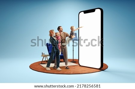 Modern lifestyle. Happy family standing in front of huge 3d model of smartphone with empty white screen isolated on blue background. New app, holiday, travel, ad concept On-line shopping, sales,
