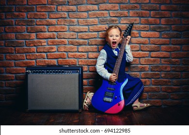 Modern little girl in school uniform posing with electric guitar over brick wall background. Rock star, rock music, pop music concept.
