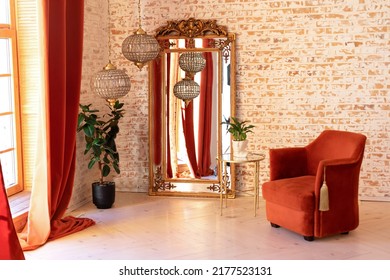 Modern Living Room In French Style. Stylish Interior With Burgundy Comfortable Armchair, Green House Plants In Pots, Coffee Table, Vintage Gold Mirror And Crystal Chandeliers Against A Brick Wall.