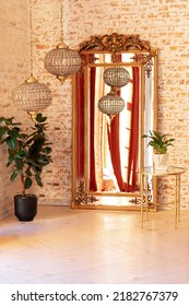 Modern Living Room In French Style. Stylish Interior With Vintage Gold Mirror, Coffee Table, Green House Plants In Pots, Decorative Ceramic Sculpture And Crystal Chandeliers Against A Brick Wall.