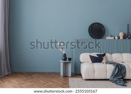 Modern living room in serene blue tones with a cozy white sofa, abstract decor, and a minimalist side table arrangement.