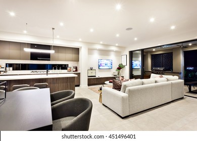 Modern Living Room With A Television And Sofas And Pillows Beside A Dining Area And Kitchen, There Is An Entrance To An Outside Patio Area