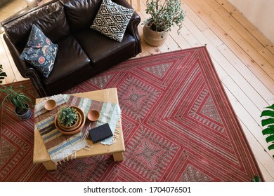 Modern Loft Living Room With High Ceiling. Leather Sofa, Wooden Table, Monstera, Book, Wicker Rug And Clay Dishes, Wooden Floor, Deer Antlers On A Red Brick Wall, Red Carpet