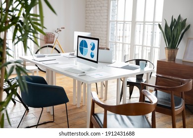 Modern Loft Office For Small Marketing Team. Empty Work Space With White Shared Table, Graphs For Financial Reports On Computer Monitors. Business Interior, Commercial Real Estate Concept