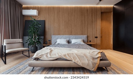 Modern loft style bedroom in apartment. Comfortable double bed with bedding and minimalistic armchair against wooden wall. Relax and sleeping concept