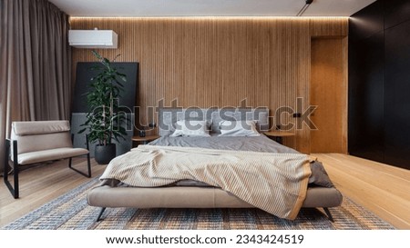 Modern loft style bedroom in apartment. Comfortable double bed with bedding and minimalistic armchair against wooden wall. Relax and sleeping concept