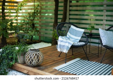 Modern lounge outdoors in backyard. Exterior veranda of house with black Acapulco armchairs and plants pots. Cozy space in patio or balcony with garland. Interior Wooden verande with garden furniture