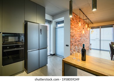 Modern Luxurious And Large Dark Gray And Black Kitchen With Kitchen Counter And Big Fridge By The Red Bick Wall