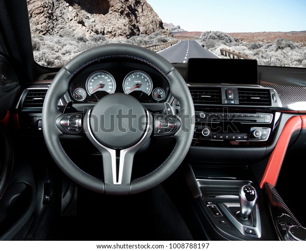Modern luxury car Interior - steering wheel, shift\
lever and dashboard. Car interior luxury.Steering wheel, dashboard,\
speedometer, display. Red and black perforated leather cockpit. Car\
on the road