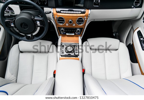 Modern luxury car white leather interior with
natural wood panel. Part of leather  seat details with stitching.
Interior of prestige modern car. White perforated leather. Car
detailing. Car inside