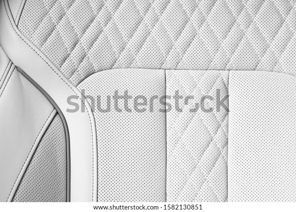 Modern luxury Car white leather interior. Part of\
perforated car seat details. White Perforated leather texture\
background. Texture, artificial leather with stitching. Perforated\
leather seats