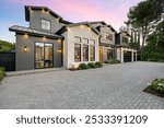 Modern luxury home exterior with a spacious driveway and well-lit facade at sunset.