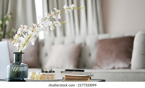 Modern Luxury Home Living Room With Comfortable Sofa, Flowers In A Ceramic Vase, Book, A Plate Of Dessert And Decor On Coffee Table. Close-up Image