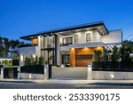 Modern luxury house exterior with large windows, landscaped yard, and evening lighting.