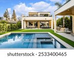 Modern luxury house with a swimming pool, outdoor seating area, and lush greenery under a bright blue sky.