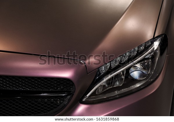 Modern luxury pink car close up. Detailed\
photo of pink-purple car. On photo is visible part of the front\
grille and headlight. The light reflects off the polished finish of\
the new luxury\
limousine.