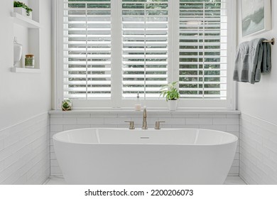 Modern luxury soaking tub with brass faucet interior design staged with plantation shutters