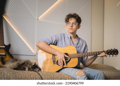 Modern Man Playing Acoustic Guitar Learning Musical Performance Sitting On Couch At Home. Teenager Male Casual Guitarist Chord Bass Solo Melody Instrumental Music Art Hobby Cultural Entertainment