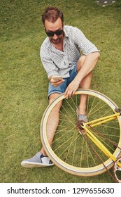 Modern man using cellphone while sitting on the grass with old bicycle.