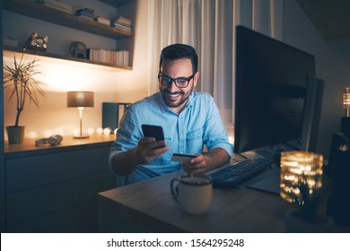 Modern man working from home at night. He is buying online and using credit card. - Shutterstock ID 1564295248