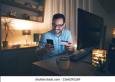 Modern man working from home at night. He is buying online and using credit card.