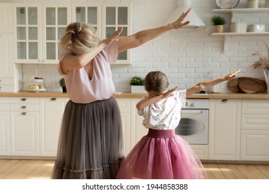 Modern Mature Grandmother And Little Granddaughter Have Fun Do Dab Gestures Dancing Together In Kitchen At Home. Elderly 60s Grandparent Granny Enjoy Weekend With Small Youth Grandchild.