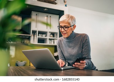 Modern mature woman using laptop and smart phone at home, portrait.