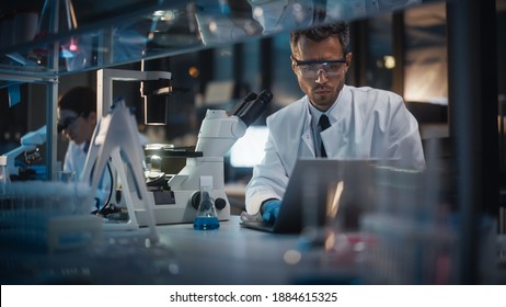 Modern Medical Research Laboratory: Male and Female Scientists Work on Laptop, Do Data Analysis, Use Microscope. Advanced Pharmaceutical Lab for Medicine, Biotechnology Development. Evening Time