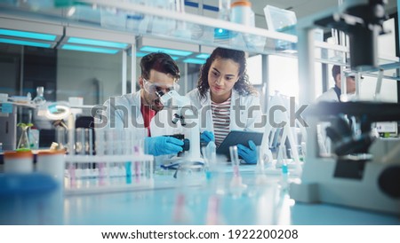 Modern Medical Research Laboratory: Portrait of Latin and Black Young Scientists Using Microscope, Digital Tablet, Doing Sample Analysis, Talking. Diverse Team of Specialists work in Advanced Lab