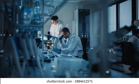 Modern Medical Research Laboratory: Two Scientists Working, Using Digital Tablet, Analyzing Test, Talking. Advanced Scientific Pharmaceutical Lab for Medicine, Biotechnology Development. Evening Time - Shutterstock ID 1884612571