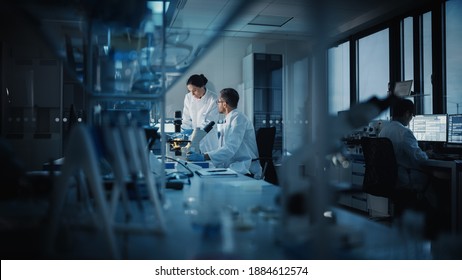 Современная медицинская исследовательская лаборатория: два ученых работают, используют цифровой планшет, анализируют тест, разговаривают. Передовая научная фармацевтическая лаборатория медицины, разработка биотехнологий. Вечернее время