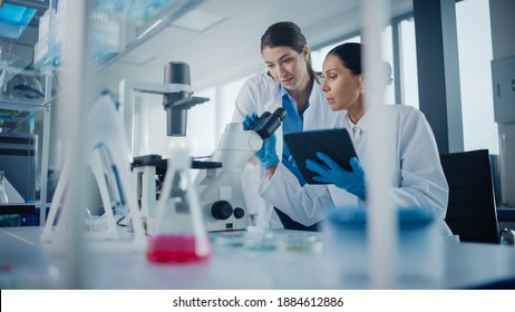 Modern Medical Research Laboratory: Two Female Scientists Working, Using Digital Tablet, Analysing Samples, Talking. Advanced Scientific Pharmaceutical Lab for Medicine, Biotechnology Development