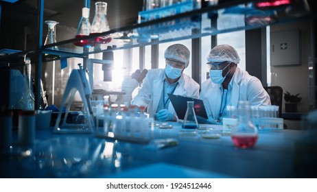 Modern Medical Research Laboratory: Two Scientists Wearing Face Masks Use Microscope, Analyse Sample In Petri Dish, Discuss Innovative Technology. Advanced Scientific Lab For Medicine, Biotechnology