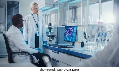 Modern Medical Research Laboratory: Two Scientists Use Computer with Screen Showing DNA Gene Analysis, Specialists Discuss Innovative Technology. Advanced Scientific Lab for Medicine, Biotechnology