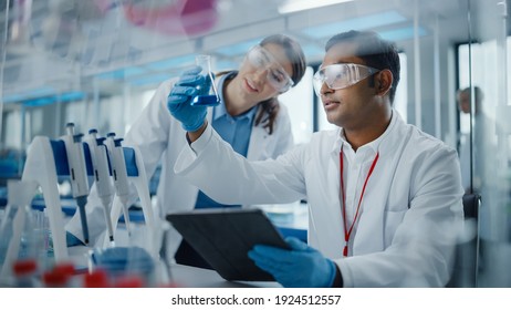 Modern Medical Research Laboratory: Two Scientists Working Together Analysing Chemicals in Laboratory Flask, Discussing Problem. Advanced Scientific Lab for Medicine, Biotechnology, Molecular Biology