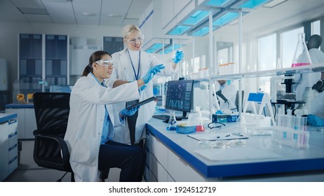 Modern Medical Research Laboratory: Two Female Scientists Working Using Digital Tablet, Analysing Biochemicals Samples. Scientific Lab For Medicine, Microbiology Development. Advanced Equipment