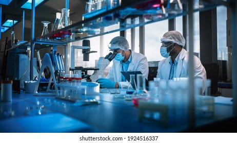 Modern Medical Research Laboratory: Two Scientists Wearing Face Masks Use Microscope, Analyse Sample In Petri Dish, Discuss Innovative Technology. Advanced Scientific Lab For Medicine, Biotechnology