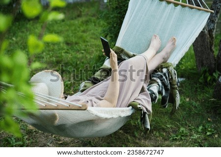 Modern Meets Rustic: Tech-Savvy Female Relaxes in Garden Hammock, Blending Nature and Digital Life