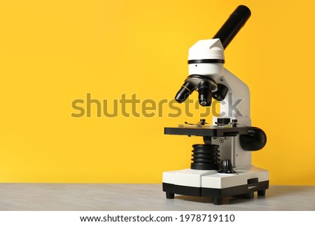 Modern microscope on table against color background
