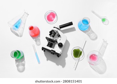 Modern microscope, petri dish and flasks with colorful liquids on white background