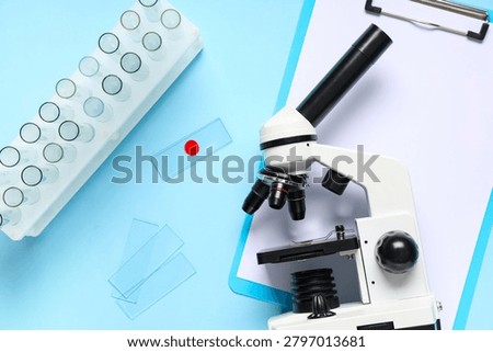 Modern microscope with test tubes, slides and clipboard on blue background