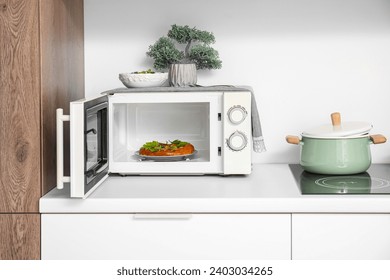 Modern microwave oven with homemade pizza on white kitchen counter