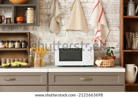 Modern microwave oven on counter near light brick wall in stylish kitchen
