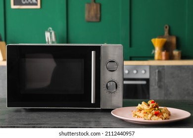 Modern Microwave Oven And Plate With Food On Table In Kitchen